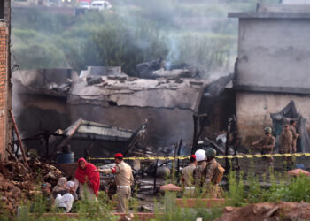 Residents sit among the rubble of their destroyed house as soldiers cordon off the site where a Pakistani Army Aviation Corps aircraft crashed in Rawalpindi on July 30, 2019. - Seventeen people were killed when a small military plane crashed into a residential area in the Pakistani city of Rawalpindi early on July 30, officials told AFP, in the latest disaster to hit the countrys troubled aviation sector. (Photo by Aamir QURESHI / AFP)