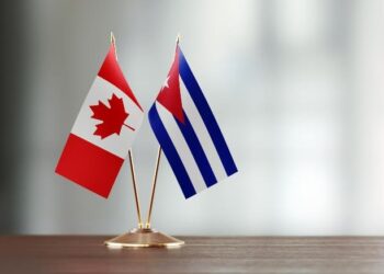 Cuban and Canadian flag pair on desk over defocused background. Horizontal composition with copy space and selective focus.