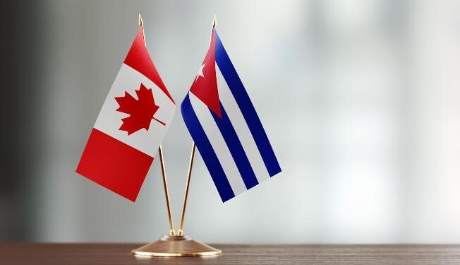 Cuban and Canadian flag pair on desk over defocused background. Horizontal composition with copy space and selective focus.