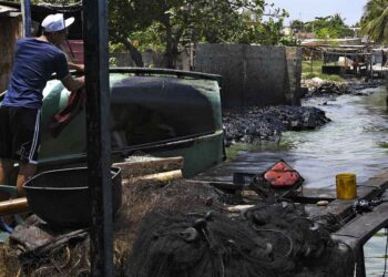 A fisherman cleans the oil smeared on his boat on the banks of the polluted Maracaibo Lake, in Cabimas, near Maracaibo, Zulia state, Venezuela, on June 13, 2019. - The city of Maracaibo is the center of the country's oil industry, and its lake is an eternal oil spill. (Photo by YURI CORTEZ / AFP)