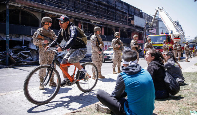 Chilean army soldiers stand guard outside a burned down Supermarket after a protest in Valparaiso, Chile, on October 20, 2019. - Chile was at a standstill on Sunday following two days of violent protests sparked by anger over economic conditions and social inequality that left three people dead, killed in the torching of a Santiago supermarket. (Photo by JAVIER TORRES / AFP)