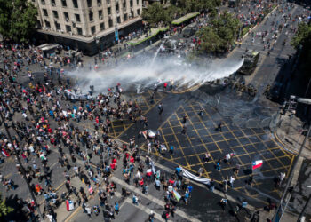 Aerial view showing riot police spraying water at demonstrators in Santiago, on the sixth straight day of street violence which erupted over a now suspended hike in metro ticket prices, on October 23, 2019. - A four-year-old child was killed during the latest round of protests against economic inequality in Chile, raising the death toll from five days of social unrest to 18 as unions launched a general strike on Wednesday. (Photo by Javier TORRES / AFP)