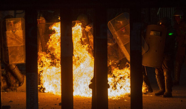 Riot police clash tto put out a fire lit by demonstrators during a protest against the government of Sebastian Pinera in Santiago on November 22, 2019. - The death toll from violent unrest in Chile rose to 23 on Friday as the country entered its fifth week of social unrest. Looting and demonstrations took place in cities across the South American nation, and an agreement on a political roadmap that will see Chile draft a new constitution has halted neither the anger, nor the bloodshed. (Photo by CLAUDIO REYES / AFP)