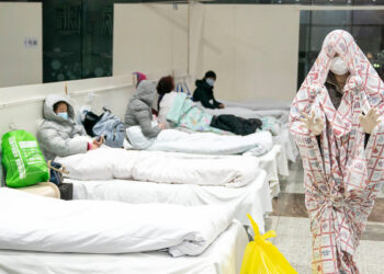 This photo taken on February 5, 2020 shows a patient (R) covered with a bed sheet at an exhibition centre converted into a hospital as it starts to accept patients displaying mild symptoms of the novel coronavirus in Wuhan in China's central Hubei province. - China scrambled to find bed space for thousands of newly infected patients on February 6, as the toll from a deadly new virus jumped again with more than 28,000 people known infected nationwide and 563 deaths. (Photo by STR / AFP) / China OUT