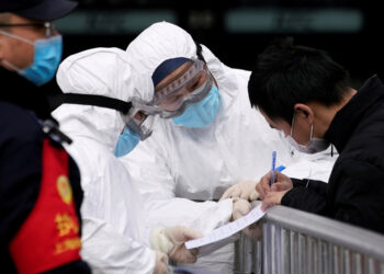 Staff members wearing protective masks check a passenger at Shanghai railway station in Shanghai, China, as the country is hit by an outbreak of a new coronavirus, February 2, 2020. REUTERS/Aly Song