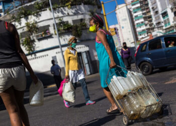 People wear face masks as a preventive measure against the global COVID-19 coronavirus pandemic as they carry water cans collected from a street pipe in Caracas, on March 27, 2020. - Venezuela is facing the novel coronavirus pandemic while suffering a major gasoline shortage and with the country's water system collapsed, which has left many homes without running water. (Photo by Cristian Hernandez / AFP)