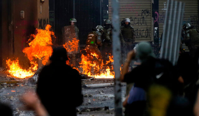 Riot police are reached by a petrol bomb during clashes with demonstrators protesting, in Santiago, on November 8, 2019. - Unrest began in Chile last October 18 with protests against a rise in transport tickets and other austerity measures that descended into vandalism, looting, and clashes between demonstrators and police. (Photo by JAVIER TORRES / AFP)