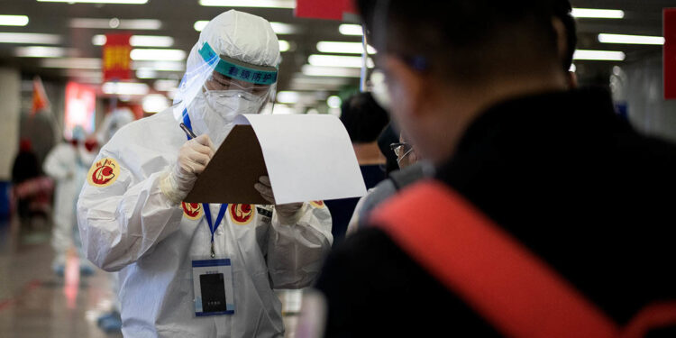 A transport personnel wearing a hazmat suit checks travellers arriving from Wuhan before guiding them to buses, which will take them to their quarantine locations, at Beijing West Railway Station on April 15, 2020. (Photo by Noel CELIS / AFP)