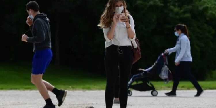 Imagen: Una mujer con mascarilla utilizando su teléfono (Getty)