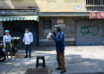 Volunteers deliver a meal bag to an elderly man as part of the "Good Neighbor Plan", in Caracas on April 28, 2020, amid the lockdown aimed at stopping the spread of the novel coronavirus. - The "Good Neighbor Plan" is an initiative started amid the new coronavirus pandemic to help elderly people without children or whose children have emigrated due to the crisis that has pushed 4,9 million Venezuelans out of the country since the end of 2015, according to the UN. (Photo by Federico PARRA / AFP)