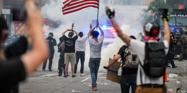 DENVER, CO - MAY 30: A man with an American flag walks toward a cloud of tear gas fired by police officers next to the Colorado State Capitol as protests against the death of George Floyd continue for a third night on May 30, 2020 in Denver, Colorado. The city of Denver enacted a curfew for Saturday and Sunday nights and Governor Jared Polis activated the Colorado National Guard in hopes of stopping protests that have wreaked havoc across the city. (Photo by Michael Ciaglo/Getty Images)