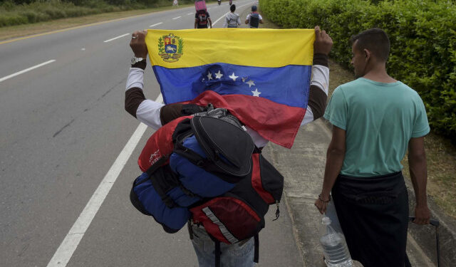 A Venezuelan migrant holding a national flag walks with other migrants on the road from Cucuta to Pamplona, in Norte de Santander Department, Colombia, on February 10, 2019. - Opposition leader Juan Guaido, recognized by some 50 countries as Venezuela's interim president, warned the military Sunday that blocking humanitarian aid from entering the country is a "crime against humanity." (Photo by Raul ARBOLEDA / AFP)