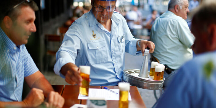 Imagen de archivo de un camarero con un escudo facial sirviendo cervezas a unos clientes en la terraza de un bar en Colonia, Alemania. 21 mayo 2020. REUTERS/Thilo Schmuelgen