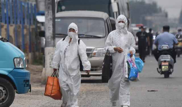 Two women wear protective suits as they walk on a street near the closed Xinfadi market in Beijing on June 13, 2020. - Eleven residential estates in south Beijing have been locked down due to a fresh cluster of coronavirus cases linked to the Xinfadi meat market, officials said on June 13. (Photo by GREG BAKER / AFP)