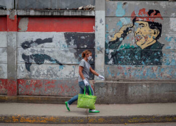 ACOMPAÑA CRÓNICA: VENEZUELA SEGURIDAD AME6549. CARACAS (VENEZUELA), 06/08/2020.- Una mujer camina frente a imágenes del expresidente venezolano Hugo Chávez el 4 de agosto de 2020 en Caracas (Venezuela). La madrugada del 13 de marzo de 2019 la Policía ingresó a la casa de Luis Alfredo Ariza en el barrio pobre de Macarao, en el oeste de Caracas, y lo detuvo bajo acusaciones que aún a la día de hoy, no están claras. Minutos después, en una calle cercana a su vivienda, lo ejecutaron de un disparo en el pecho. EFE/RAYNER PEÑA R.