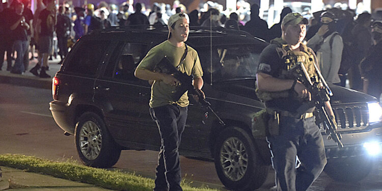 Kyle Rittenhouse, left, with backwards cap, walks along Sheridan Road in Kenosha, Wis., Tuesday, Aug. 25, 2020, with another armed civilian. Prosecutors on Thursday, Aug. 27, 2020 charged Rittenhouse, a 17-year-old from Illinois in the fatal shooting of two protesters and the wounding of a third in Kenosha, Wisconsin, during a night of unrest following the weekend police shooting of Jacob Blake. (Adam Rogan/The Journal Times via AP)