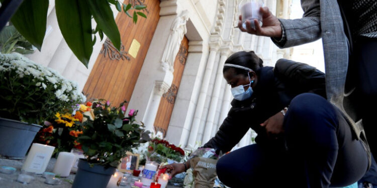 A woman lights a candle in front of the Notre-Dame de l'Assomption Basilica in Nice on October 30, 2020 during a tribute to the victims killed by a knife attacker the day before. - A 47-year-old man believed to have been in contact with the suspected knifeman who killed three at a church in Nice has been detained for questioning, a judicial source said on October 30, 2020. The man was detained late Thursday after the attack at the city's Notre-Dame basilica by a 21-year-old Tunisian who arrived in France on October 9. (Photo by Valery HACHE / AFP)