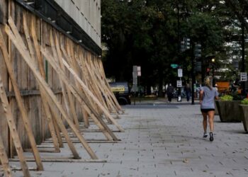 Una mujer trota delante de tablas de madera levantadas para proteger comercios en Estados Unidos durante las elecciones. Foto: REUTERS/Leah Millis.