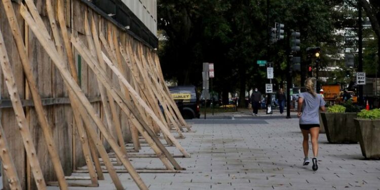 Una mujer trota delante de tablas de madera levantadas para proteger comercios en Estados Unidos durante las elecciones. Foto: REUTERS/Leah Millis.