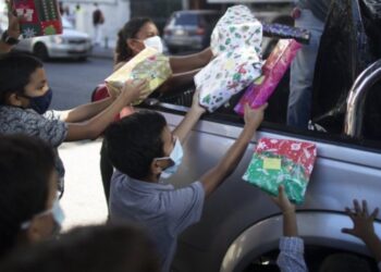 Los niños reciben regalos de Navidad donados por el grupo de voluntarios “Un Juguete, Una Buena Noticia” desde la parte trasera de una camioneta en Caracas, Venezuela, el viernes 18 de diciembre de 2020. (AP Foto/Ariana Cubillos).