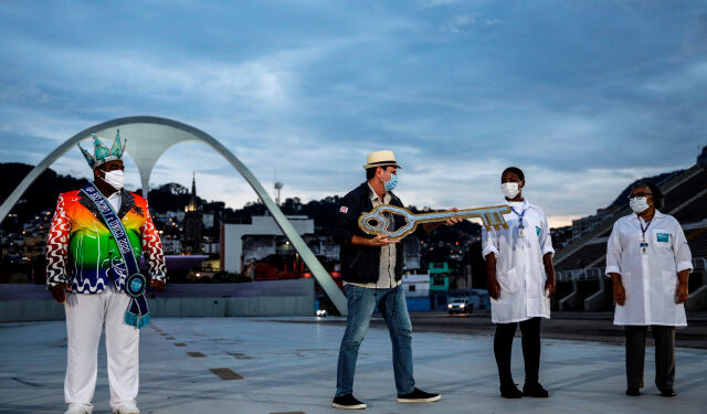 AME5415. RIO DE JANEIRO (BRASIL), 12/02/2021.- El alcalde de Río de Janeiro, Eduardo Paes (c), entrega la llave de la ciudad a dos enfermeras como símbolo y homenaje a los trabajadores de la salud que enfrentan la pandemia hoy, durante un evento en el Sambódromo del carnaval de Río, vacío e iluminado hoy, en Río de Janeiro (Brasil). El Sambódromo, que permanecerá vacío y silencioso entre este viernes y el miércoles de ceniza por la cancelación del Carnaval más famoso de Brasil debido a la pandemia de la covid, contará con una iluminación especial por las noches en homenaje a las víctimas del coronavirus. El espectáculo de luces, simulando un desfile carnavalesco y destacando los diferentes colores de las escuelas de samba cariocas, fue encendido este viernes por el alcalde de Río de Janeiro, Eduardo Paes, en una ceremonia en la que también se rindió tributo a las víctimas de la pandemia. EFE/ Antonio Lacerda