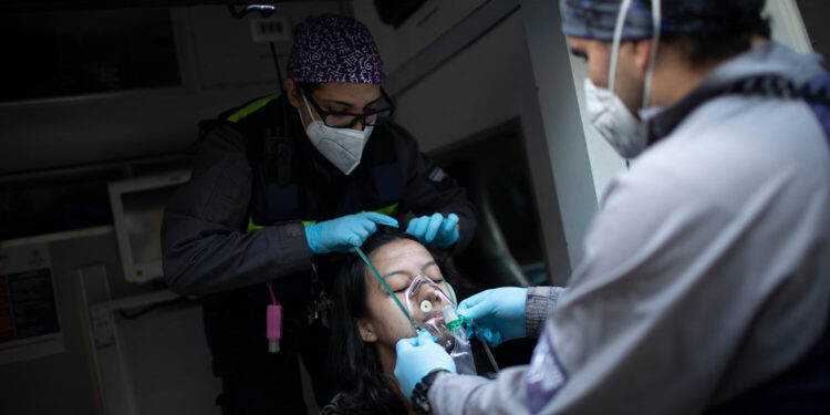 Wearing masks as a precaution against the new coronavirus, Angels of the Road volunteer paramedics Rodolfo Alvarado, right, and Zully Rodiz, place an oxygen mask on a woman who was in a residential building when a car burst into flames in the parking lot, in Caracas, Venezuela, Monday, Feb. 8, 2021. Despite receiving no paychecks, the roughly 40 volunteer paramedics are ready at a moment's notice to jump onto motorcycles and fire up their single ambulance and race into the streets to attend an emergency. (AP Photo/Ariana Cubillos)