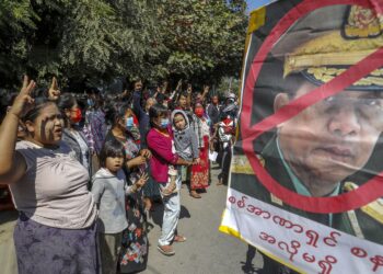 Demonstrators shout slogan and flash three-fingered salute, a symbol of resistance against the military coup standing next to a defaced image of Myanmar military Commander-in-Chief Senior Gen. Min Aung Hlaing in Mandalay, Myanmar on Wednesday, Feb. 10, 2021. Protesters continued to gather Wednesday morning in Mandalay breaching Myanmar's new military rulers' decrees that effectively banned peaceful public protests in the country's two biggest cities. (AP Photo)