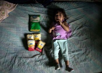 Retrato de Adriana López Guzmán, de un año, el 25 de enero de 2020, en su vivienda en el barrio La Vega de Caracas (Venezuela). Junto a Adriana se puede ver 1 kilo de arroz y 2 kilos de harina de maíz que su madre, Yulitza Guzmán, pudo comprar por Bs. 200.000 (10 centavos de dólar). Foto EFE Miguel Gutiérrez