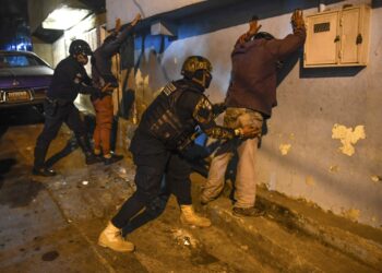 Members of the Venezuelan Scientific Police (CICPC) frisk men during an operation amid the COVID-19 pandemic in Los Teques, Miranda state, Venezuela, on March 20, 2021. - In Miranda there is a circulation restriction since 18h00, there is the order to close stores at 16h00, to wear face masks and to prevent meetings of more than five people, amid a second wave of the COVID-19 pandemic. (Photo by Federico PARRA / AFP)