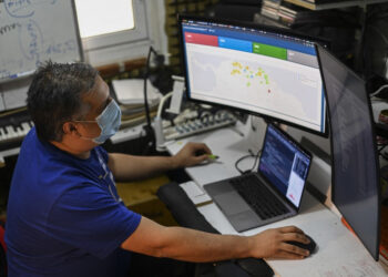 Venezuelan Jose Miguel Avendano, works on his computers as he shows an application designed by him that allows locating health centers and hospitals as well as the most feasible route to reach them in the case of emergencies due to the COVID-19 in the La Candelaria neighborhood, Caracas on May 11, 2021. - A database of clinics and hospitals, a biosecurity catalogue for businesses or a medicine and oxygen directory. Apps created by Venezuelans against COVID-19 emerge amidst the economic crisis and a virulent second wave of contagions. (Photo by Yuri CORTEZ / AFP)