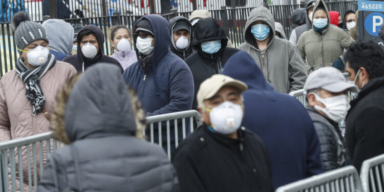 Patients wear personal protective equipment while maintaining social distancing as they wait in line for a COVID-19 test at Elmhurst Hospital Center, Wednesday, March 25, 2020, in New York. Gov. Andrew Cuomo sounded his most dire warning yet about the coronavirus pandemic Tuesday, saying the infection rate in New York is accelerating and the state could be as close as two weeks away from a crisis that sees 40,000 people in intensive care. Such a surge would overwhelm hospitals, which now have just 3,000 intensive care unit beds statewide. (AP Photo/John Minchillo)