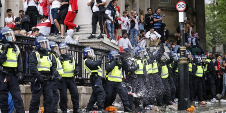 A line of police officers are the target of beer can throwers as England supporters stand around the edges of Trafalgar Square during a live screening of the UEFA EURO 2020 final football match between England and Italy in central London on July 11, 2021. (Photo by Tolga Akmen / AFP)