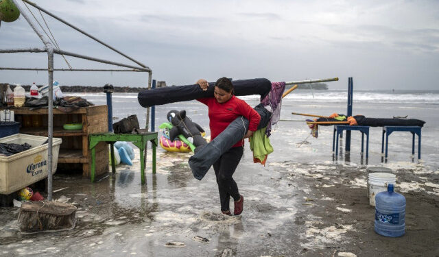 A woman removes umbrellas from the beach as strong waves reach the coast due to Hurricane Grace, which has reached category 2, in Boca del Rio, Veracruz, Mexico, on August 20, 2021. - Grace regained hurricane strength Friday as it barreled towards Mexico for a second time, triggering warnings of flooding and mudslides in mountains on the eastern mainland. (Photo by VICTORIA RAZO / AFP)