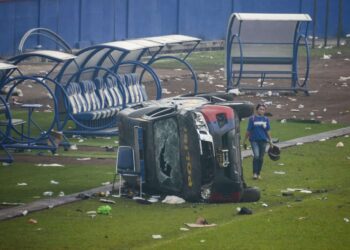 Una mujer pasa junto a un vehículo de la policía destrozado tras los disturbios en un partido de fútbol en el estadio Kanjuruhan de Malang, que han dejado al menos 174 muertos. El brote de violencia se produjo después de que cerca de 3.000 aficionados del equipo Arema irrumpieran en el campo tras la derrota 2-3 sufrida ante el rival Persebaya Surabaya y chocaran con las fuerzas de seguridad, que a su vez utilizaron gases lacrimógenos en un intento de dispersar la multitud. EFE/ Sandi Sadewa