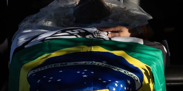 ATENCIÓN EDITORES: CONTENIDO GRÁFICO EXPLÍCITO - BRA01. SANTOS (BRASIL), 02/01/2023.- Una bandera nacional de Brasil y una del club Santos envuelven el cuerpo de la leyenda del fútbol Pelé, durante su velatorio hoy, en el estadio de Vila Belmiro en la ciudad de Santos (Brasil). El velatorio de Pelé, fallecido el pasado jueves a los 82 años, comenzó este lunes para que los aficionados brasileños rindan homenaje al mítico delantero, considerado por muchos el mejor futbolista de la historia. La ceremonia se celebra en el césped del estadio Vila Belmiro, en la ciudad de Santos, donde "O Rei" jugó como local la mayor parte de su carrera deportiva, con la presencia del presidente de la FIFA, Gianni Infantino, y de otras personalidades del mundo del fútbol. EFE/ Isaac Fontana ATENCIÓN EDITORES: CONTENIDO GRÁFICO EXPLÍCITO