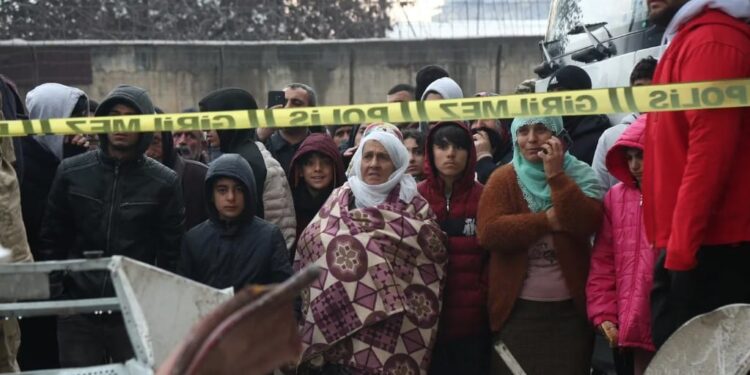 Víctimas del terremoto se juntan tras una cinta policial mientras ven el desastre que quedó en Diyarbakir, Turquía.