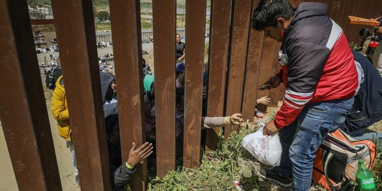 Repartidores de comida rápida entregan pedidos a migrantes en el muro fronterizo hoy, en la ciudad de Tijuana, Baja California (México). Los repartidores de comida rápida en la ciudad mexicana de Tijuana comenzaron a llegar este jueves a los linderos del campamento entre los muros fronterizos, donde pernoctan alrededor de 400 migrantes de diversas nacionalidades, incrementando los precios de los productos hasta los 100 dólares. EFE/Joebeth Terríquez