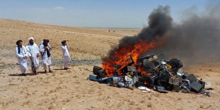 In this handout photograph taken on July 29, 2023 and released by the Afghanistan's Ministry for the Propagation of Virtue and the Prevention of Vice, members of Taliban stand guard after setting fire to a pile of musical instruments and equipments on the outskirts of Herat. Authorities from Afghanistan's vice ministry created a bonfire of confiscated musicial instruments and equipment in Herat province at the weekend, deeming music immoral. (Photo by Afghanistan's Ministry for the Propagation of Virtue and the Prevention of Vice / AFP) / RESTRICTED TO EDITORIAL USE - MANDATORY CREDIT "AFP PHOTO/Afghanistan's Ministry for the Propagation of Virtue and the Prevention of Vice" - NO MARKETING NO ADVERTISING CAMPAIGNS - DISTRIBUTED AS A SERVICE TO CLIENTS