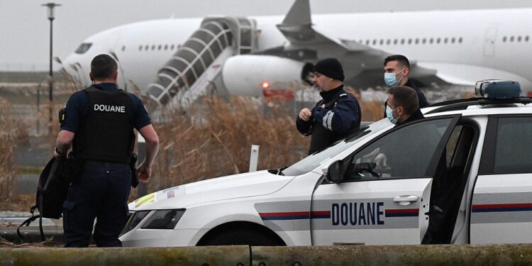 French customs officers stand next to a customs car with an Airbus A340 in the background which was grounded on the tarmac since December 21 over suspected "human trafficking", at the Vatry airport, north-eastern France on December 25, 2023. Two Indians passengers on the flight grounded since December 21, in the Marne region of France on suspicion of human trafficking will be presented to an examining magistrate on December 25, with possible indictment, while most of the other passengers are due to take off for India later on December 25. (Photo by FRANCOIS NASCIMBENI / AFP)