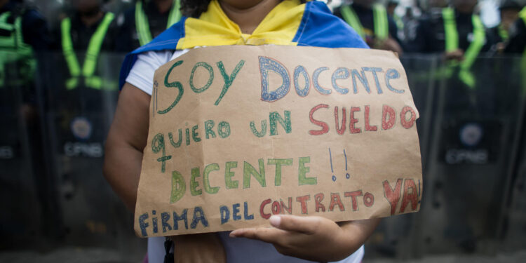 AME082. CARACAS (VENEZUELA), 15/01/2024.- Una mujer sostiene un cartel de protesta durante una manifestación de maestros, respaldados por trabajadores de otros sectores, contra los bajos salarios y para exigir mejoras laborales, hoy, en Caracas (Venezuela). Cientos de maestros en Venezuela volvieron a las calles este lunes, cuando se conmemora su día en el país, con el objetivo de exigir al Gobierno de Nicolás Maduro la reanudación de las negociaciones para una nueva convención colectiva. Esta es la segunda jornada de manifestaciones de trabajadores de este año, que comenzaron el pasado 9 de enero. EFE/ Miguel Gutiérrez