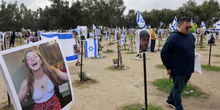 A man walks past portraits of Israeli people taken captive or killed by Hamas militants during the October 7 attacks, during a visit at the site where the Supernova music festival took place near Kibbutz Reim in southern Israel, on January 14, 2024, after 100 days of war between Israel and the militant Hamas group in Gaza. (Photo by Menahem Kahana / AFP)