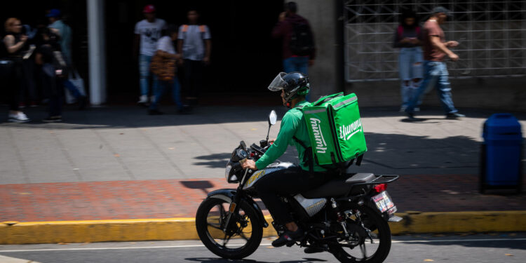 AME5448. CARACAS (VENEZUELA), 05/03/2024.- Un repartidor de servicio a domicilio conduce su motocicleta por una calle el 4 de marzo de 2024, en Caracas (Venezuela). El reparto a domicilio registra un crecimiento sostenido desde 2020 en Venezuela, donde miles de personas han mejorado sus ingresos luego de haberse sumado a este sector, que recientemente logró echar atrás una serie de medidas que buscaban su regulación, como el cobro del 1 % sobre estos servicios. Datos suministrados a EFE por la Cámara Venezolana de Comercio Electrónico (Cavecom-e) dan cuenta de más de 200.000 repartidores con motocicletas -el principal medio de transporte usado en el país para estas entregas- incorporados al sector del 'delivery'. EFE/ Rayner Peña R.