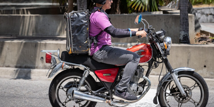 AME5448. CARACAS (VENEZUELA), 05/03/2024.- Un repartidor de servicio a domicilio conduce su motocicleta por una calle el 4 de marzo de 2024, en Caracas (Venezuela). El reparto a domicilio registra un crecimiento sostenido desde 2020 en Venezuela, donde miles de personas han mejorado sus ingresos luego de haberse sumado a este sector, que recientemente logró echar atrás una serie de medidas que buscaban su regulación, como el cobro del 1 % sobre estos servicios. Datos suministrados a EFE por la Cámara Venezolana de Comercio Electrónico (Cavecom-e) dan cuenta de más de 200.000 repartidores con motocicletas -el principal medio de transporte usado en el país para estas entregas- incorporados al sector del 'delivery'. EFE/ Rayner Peña R.