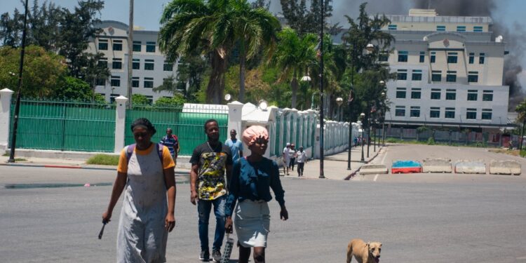 As smoke billows from the Ministry of Finance building behind them, people leave the area after hearing gunshots from armed gangs near the National Palace in Port-au-Prince, Haiti, on April 2, 2024. More than 50,000 people fled Port-au-Prince within three weeks last month as an explosion of gang violence shook the Haitian capital, the United Nations said April 2, 2024. (Photo by Clarens SIFFROY / AFP)