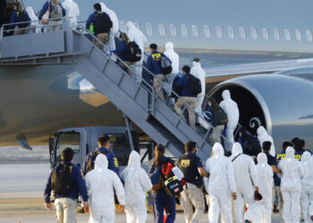 Venezuelan and Colombian migrants being deported wear protective gear amid the COVID-19 pandemic as they walk in a line with police to board a plane at General Diego Aracena Aguilar International Airport in Iquique, Chile, Wednesday, Feb. 10, 2021. In recent weeks the border town of Colchane, on the border with Bolivia, has received a significant increase in immigrants, especially Venezuelans who have been walking from their country of origin to meet with family members in Chile or pushed out by quarantines in Peru. (Alex Diaz/Aton Chile via AP)