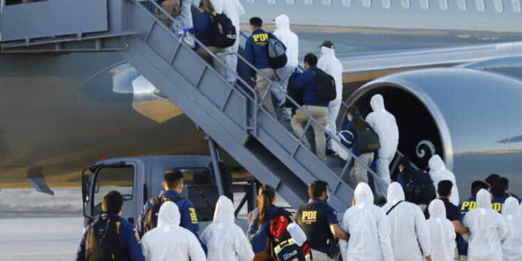 Venezuelan and Colombian migrants being deported wear protective gear amid the COVID-19 pandemic as they walk in a line with police to board a plane at General Diego Aracena Aguilar International Airport in Iquique, Chile, Wednesday, Feb. 10, 2021. In recent weeks the border town of Colchane, on the border with Bolivia, has received a significant increase in immigrants, especially Venezuelans who have been walking from their country of origin to meet with family members in Chile or pushed out by quarantines in Peru. (Alex Diaz/Aton Chile via AP)
