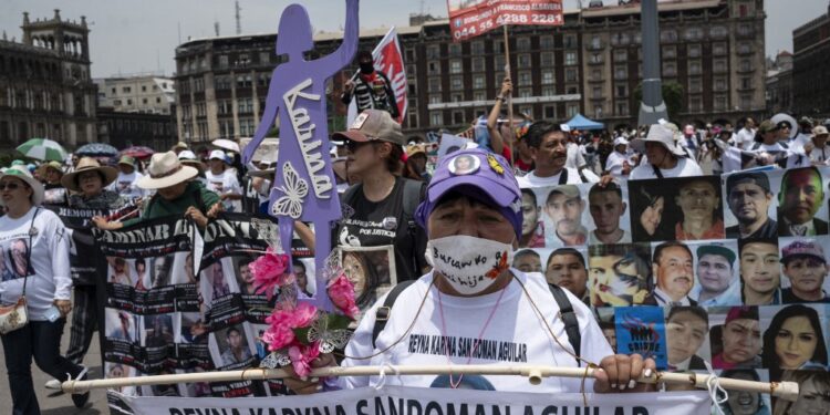 Mothers and relatives of missing persons in different states of Mexico carry signs with photos of their loved ones while participating in a march to demand that the government clarify the disappearances within the framework of Mother's Day in front of the National Palace at El Zocalo Square in Mexico City on May 10, 2024. (Photo by Yuri CORTEZ / AFP)