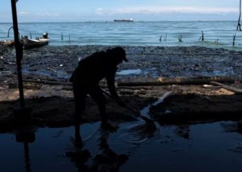 Un hombre retira agua sucia del interior de una choza de paja instalada en la orilla del Lago de Maracaibo contaminado con basura y derrames de petróleo, en San Francisco, Venezuela, el jueves 10 de agosto de 2023 (AP Foto/Ariana Cubillos)