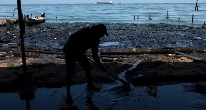 Un hombre retira agua sucia del interior de una choza de paja instalada en la orilla del Lago de Maracaibo contaminado con basura y derrames de petróleo, en San Francisco, Venezuela, el jueves 10 de agosto de 2023 (AP Foto/Ariana Cubillos)