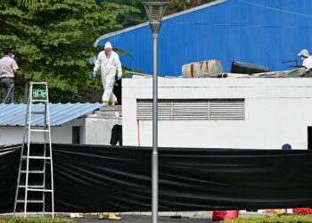 A forensic worker walks on top of a container inside the city morgue in Guayaquil, Ecuador on June 13, 2024. - In the surroundings of Guayaquil's morgue, the mourners must not only deal with their loss, but with the nauseating smell from the forensic center, packed with bodies, many, victims of a painful war imposed by drug trafficking in Ecuador. (Photo by MARCOS PIN / AFP)